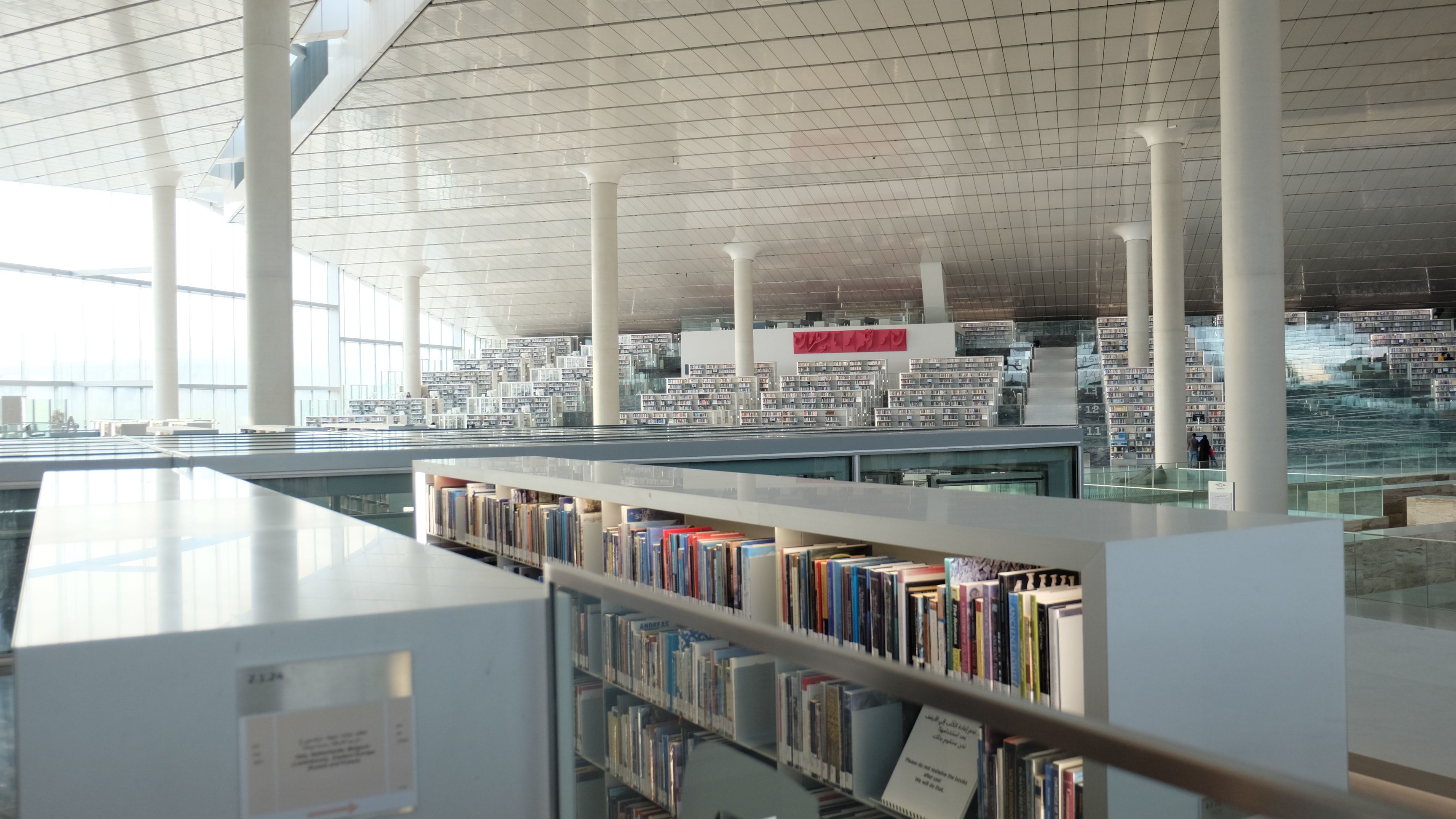 Interior of the contemporary Qatar National library, with a high ceiling and natural light filled with white bookshelves.