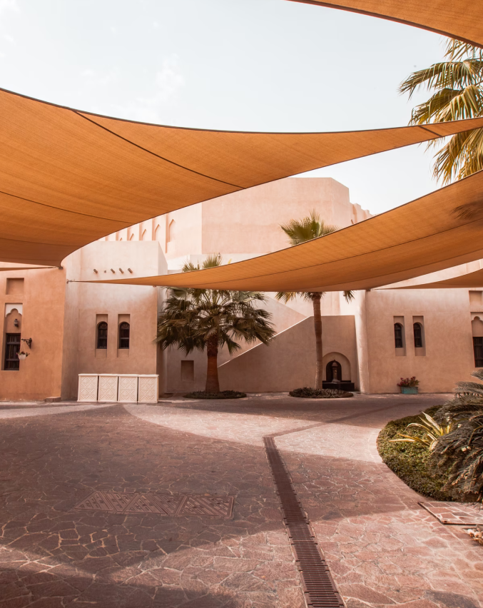 Katara Cultural village in Doha on a bright sunny day, with canopies for shade and several palm trees.