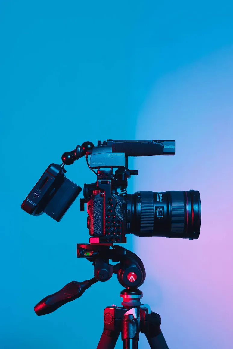 A professional camera set up on a tripod, seen from the side against a blue and pink background.