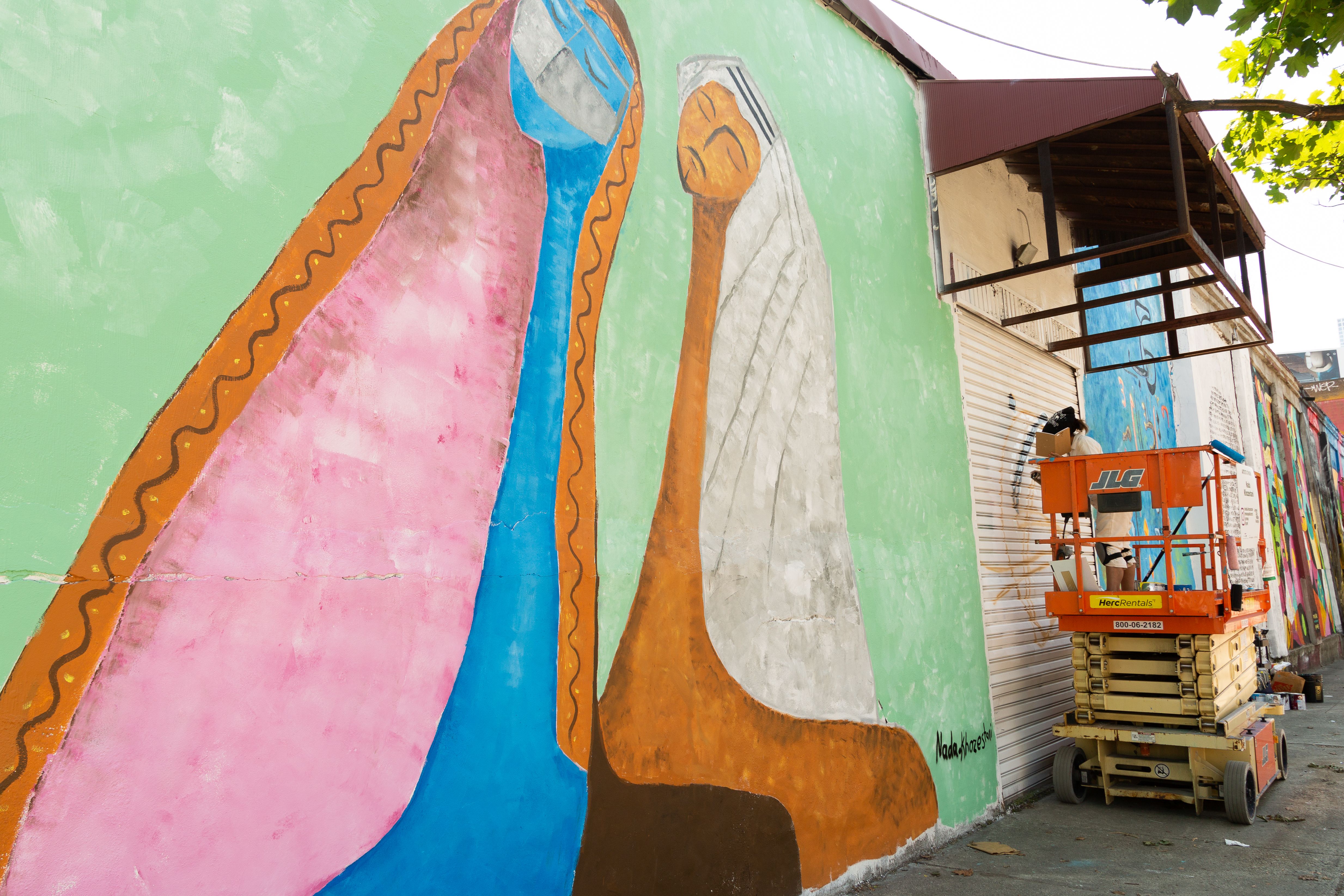 A mural depicting a man and a woman wearing traditional Qatari headwear painted in bright colours against a green background.