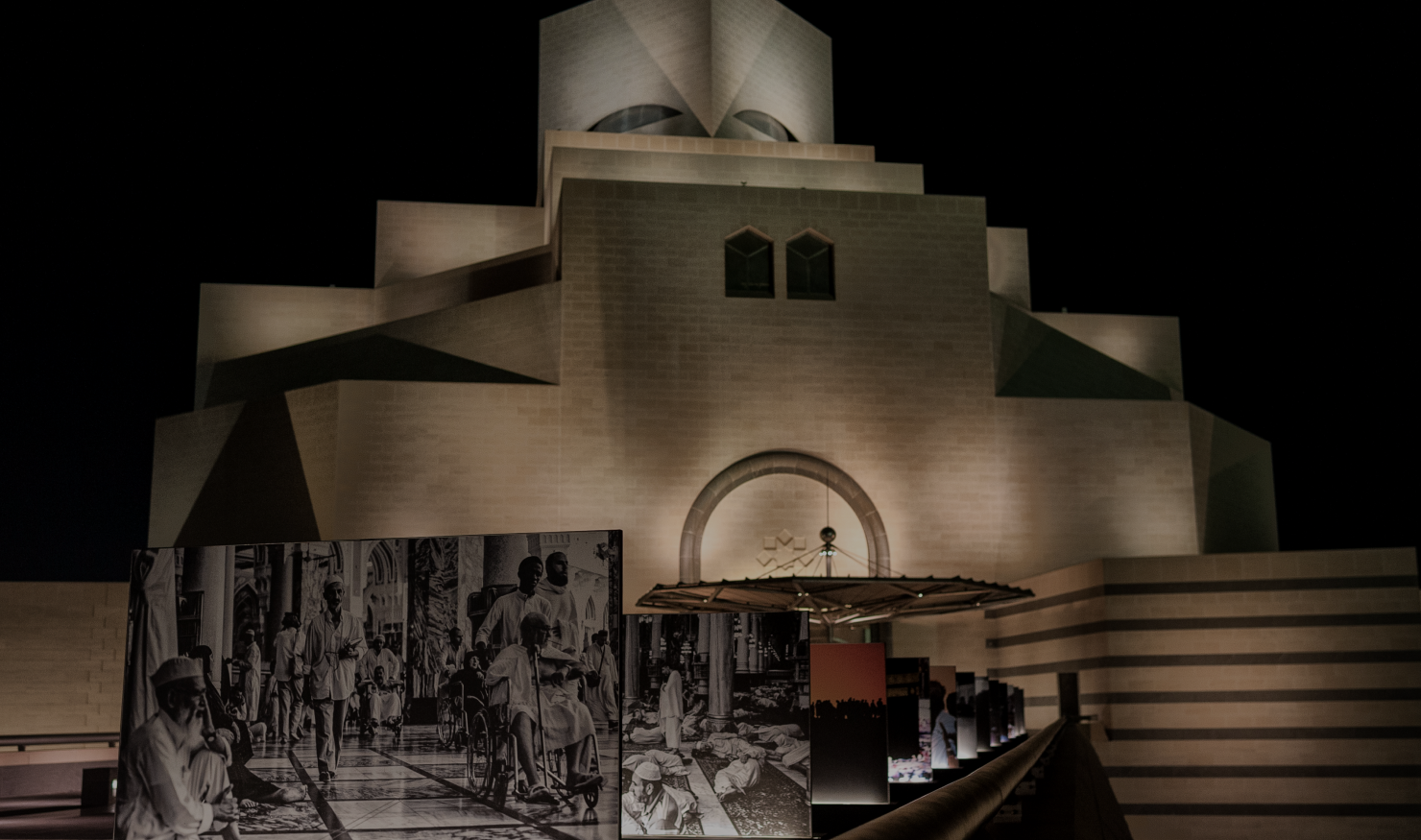 Museum of Islamic Art lit up at night, with large photos printed on panels leading to the entrance.